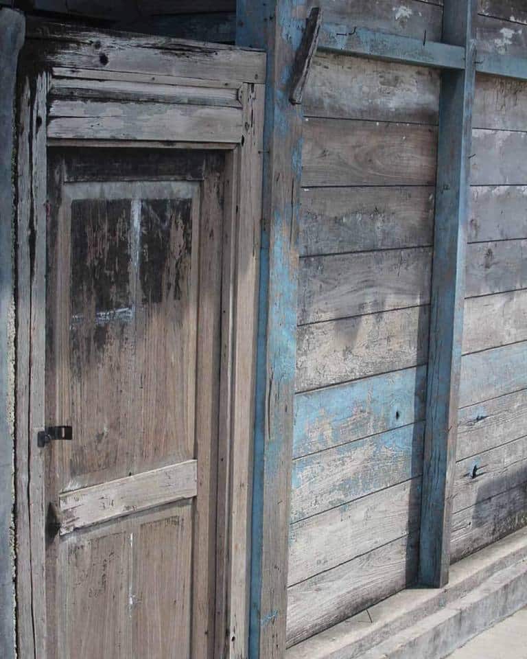 Weathered timber door and wall boards with surface marks and traces of blue paint