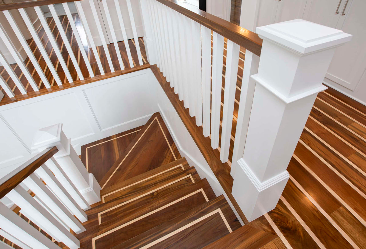 Striped wood floor meets a turning staircase with white balusters and pale-edged treads