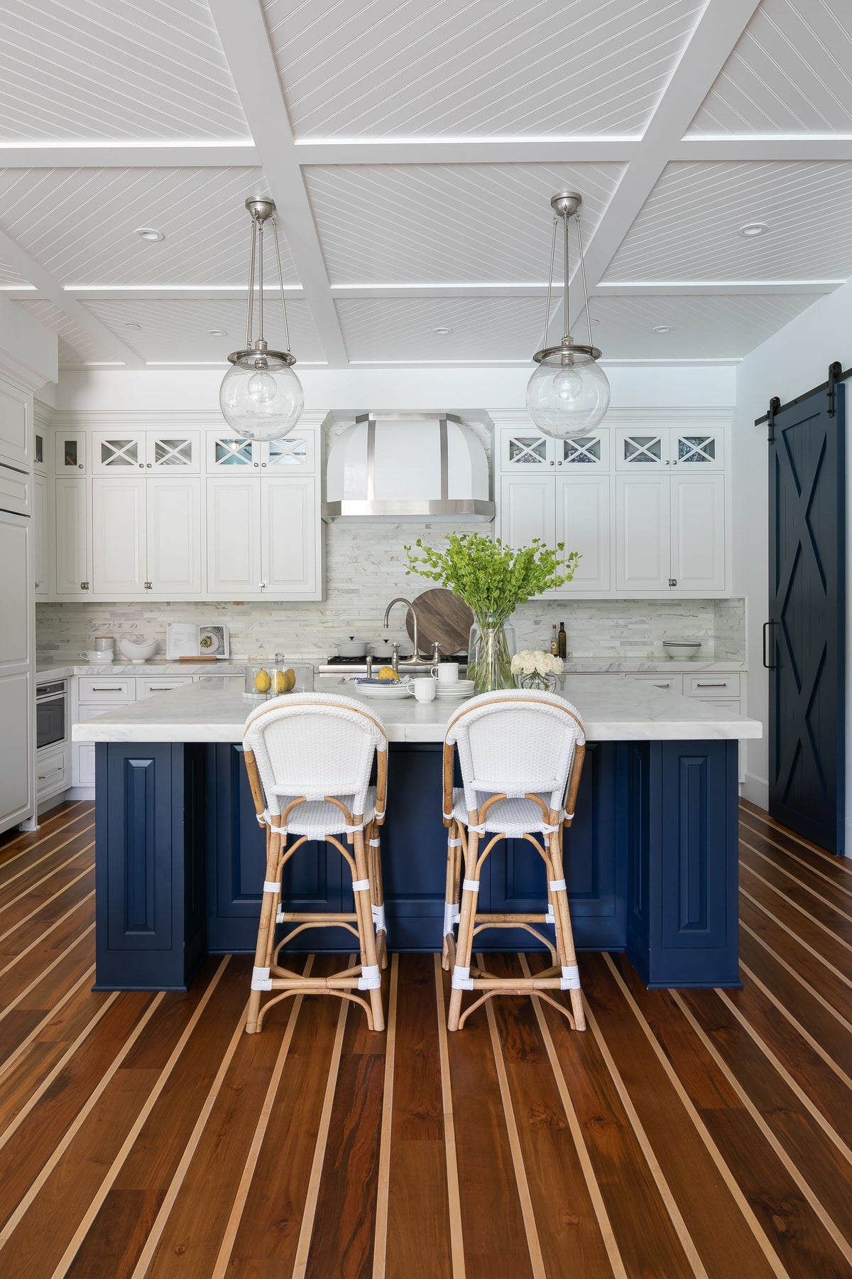 Striped wood floor around a navy kitchen island, with white cabinets and glass pendants
