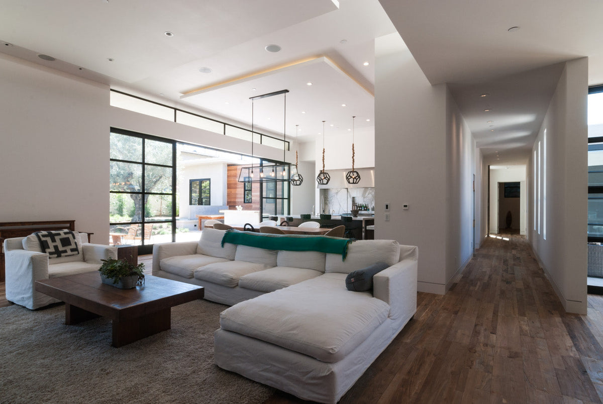 Open-plan living room and kitchen with wood floor, white sectional, and green island stools