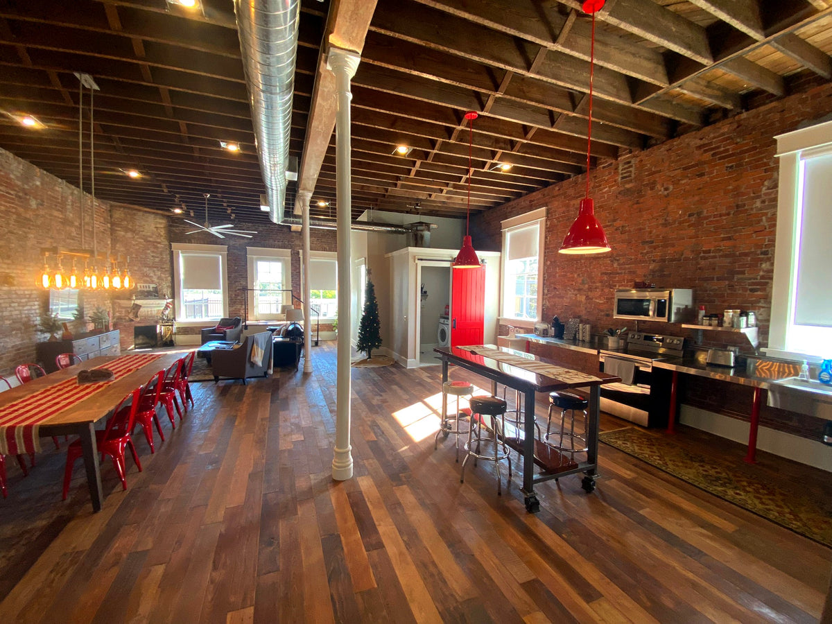Long loft dining space with varied brown floorboards, exposed brick, timber ceiling, and metal duct