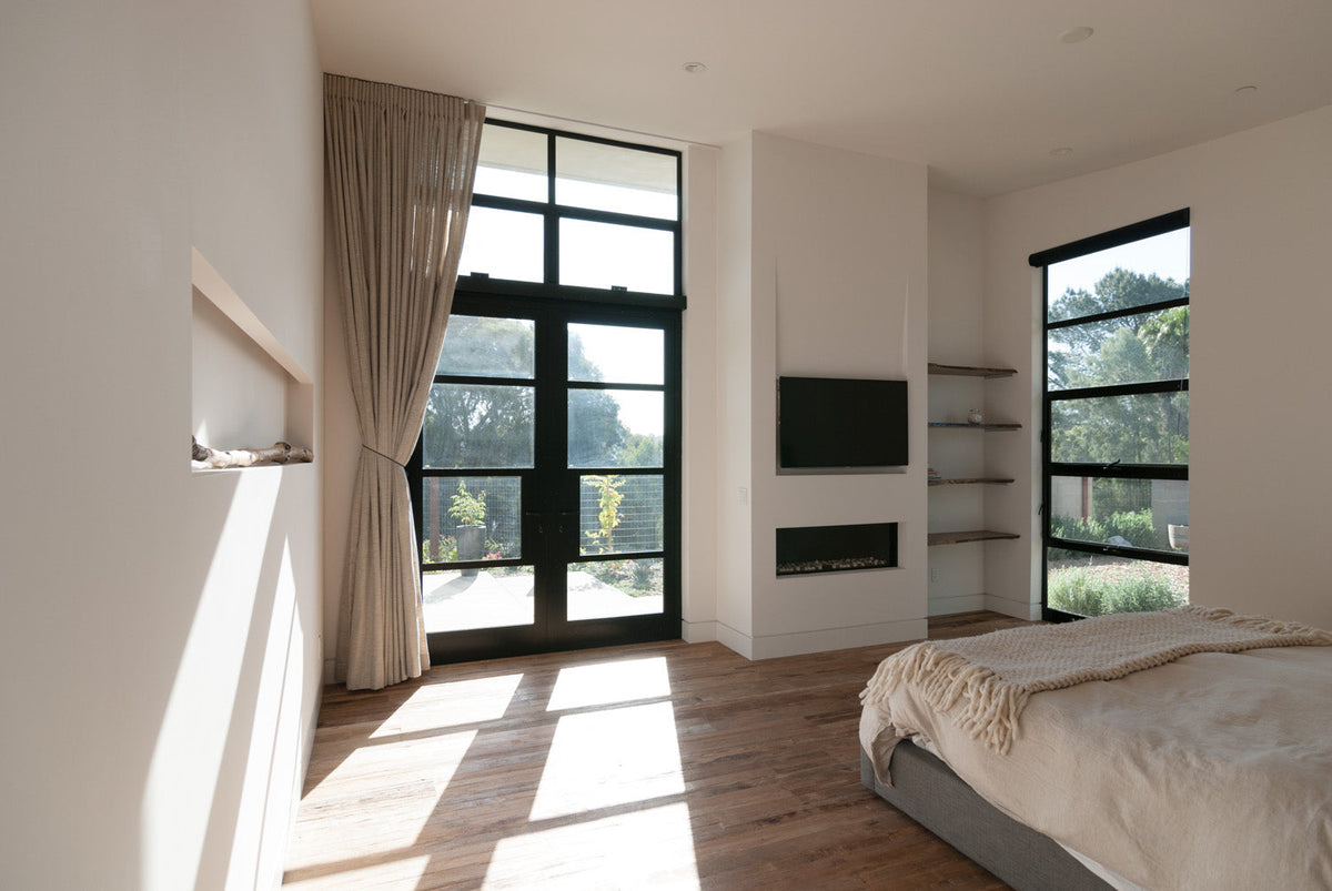 Bright bedroom with varied wood flooring beneath a low bed and black-framed windows