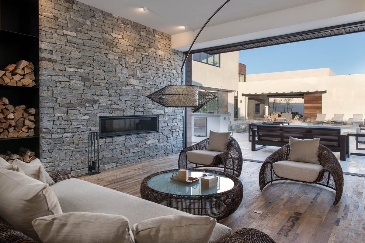Living room with stone fireplace, wood flooring, round tables, and open terrace