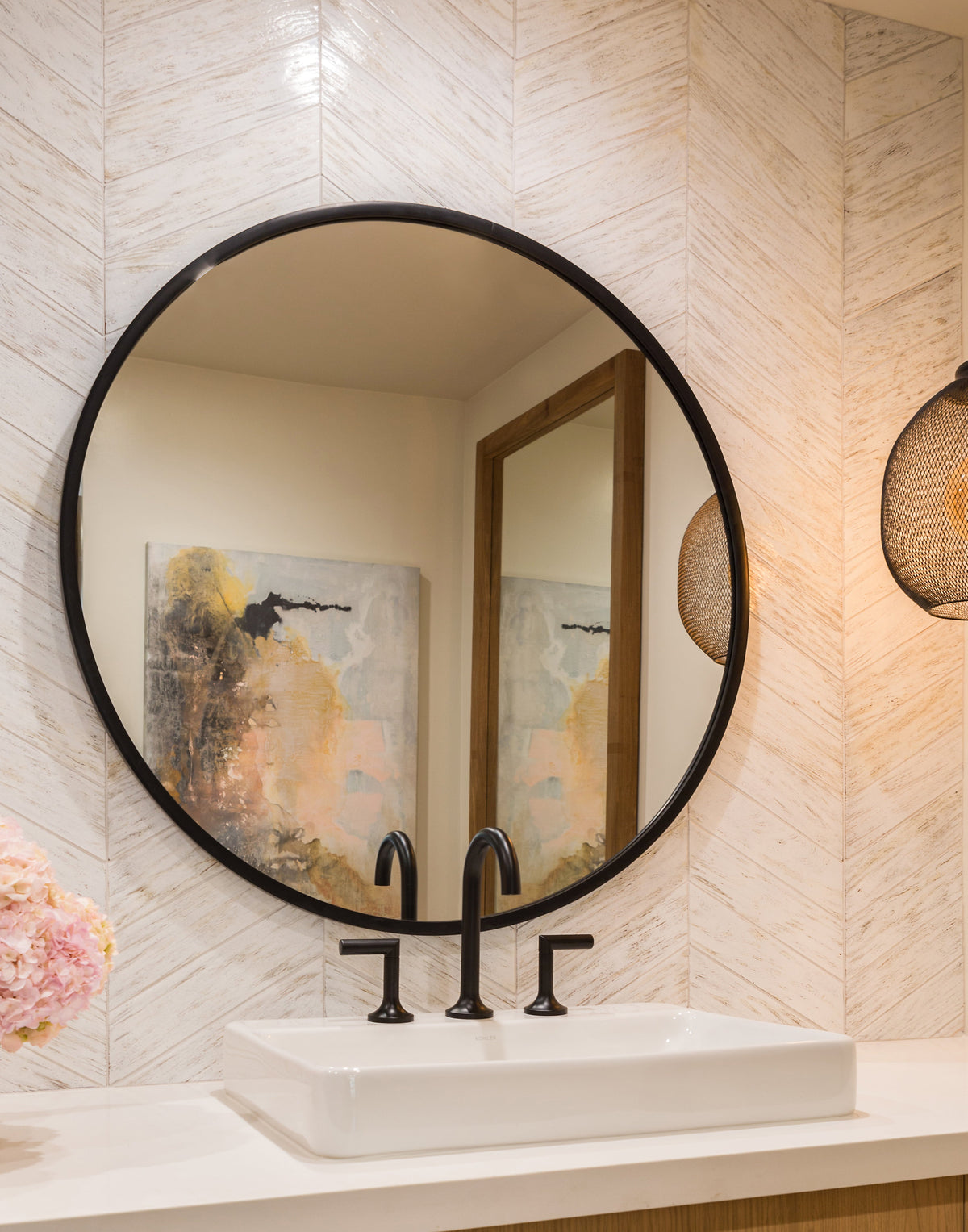 Light-colored chevron wall beside a lit sconce and round mirror