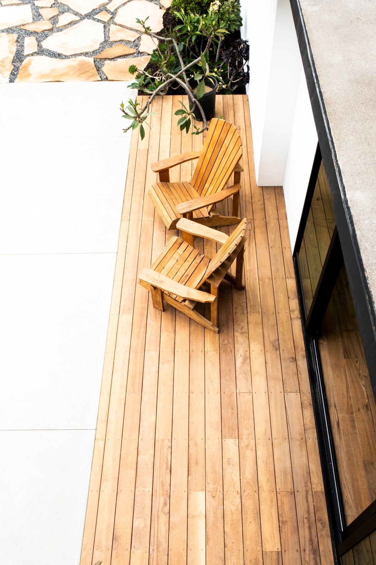 Two timber chairs on a narrow wood deck beside a white wall and a dark glazed door
