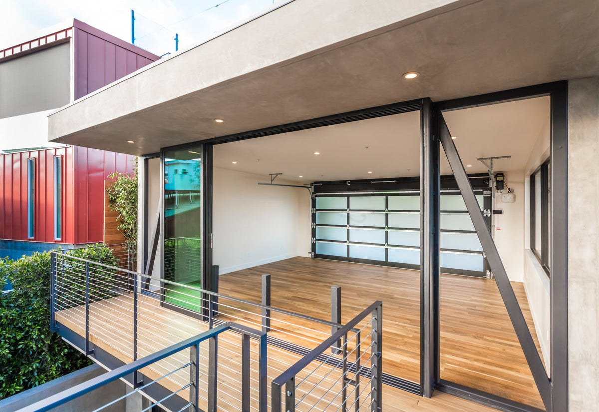 An upper-level wood deck outside open folding glass doors with metal railings