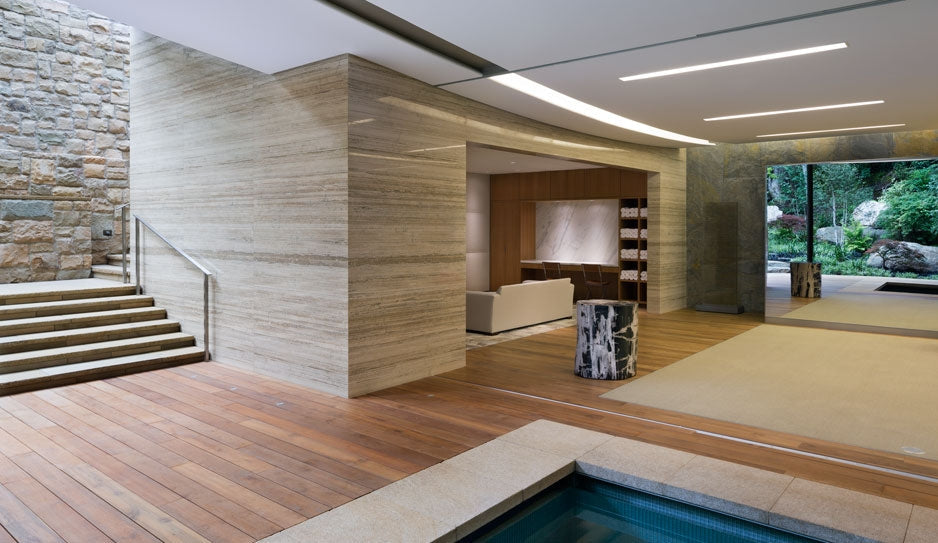 Wood decking meets a rectangular pool edge inside an open-sided pavilion