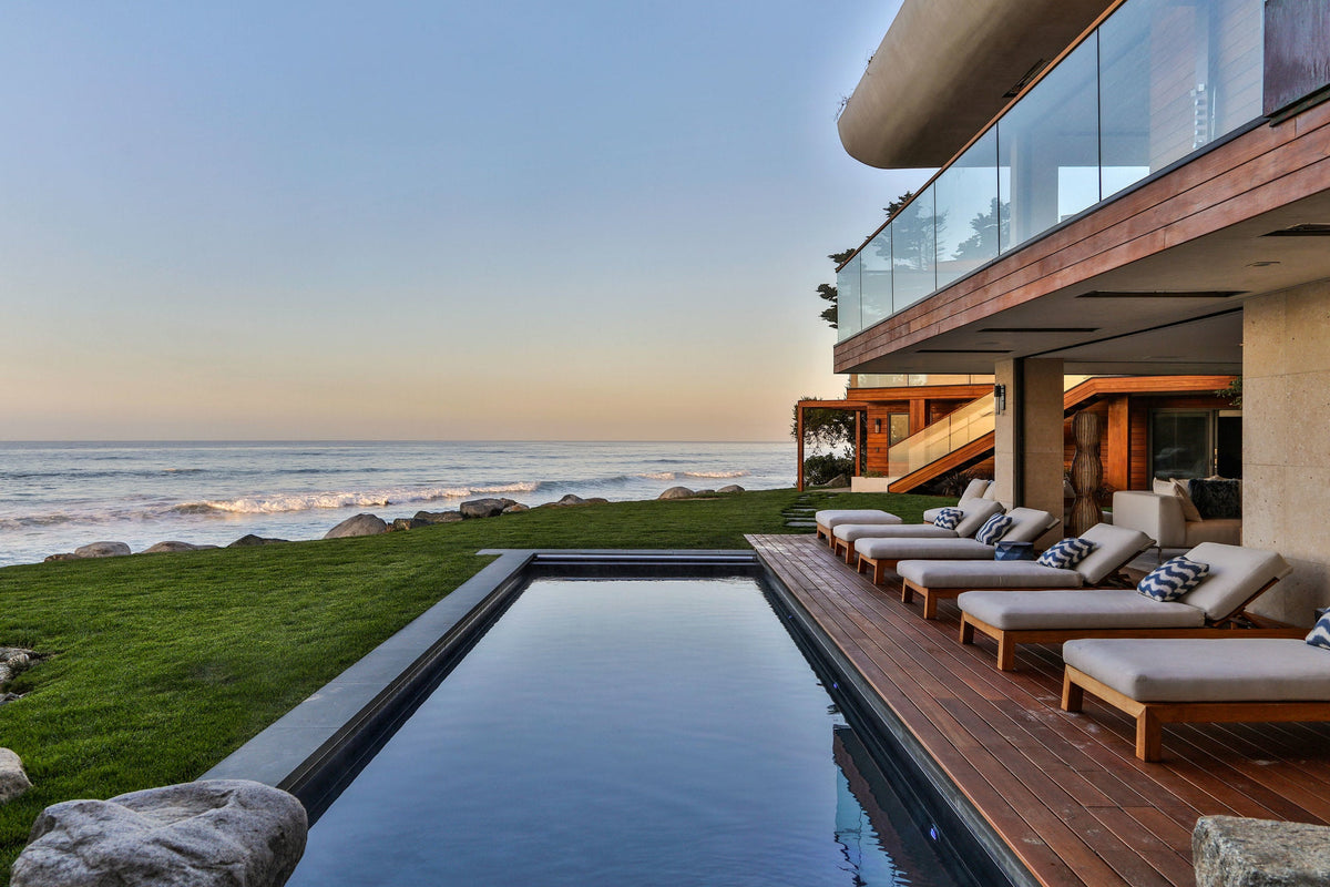 An oceanfront pool and wood deck with outdoor seating beside a modern house