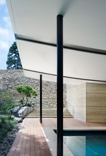 A narrow wood deck sits beside stone walls, planting and a pool