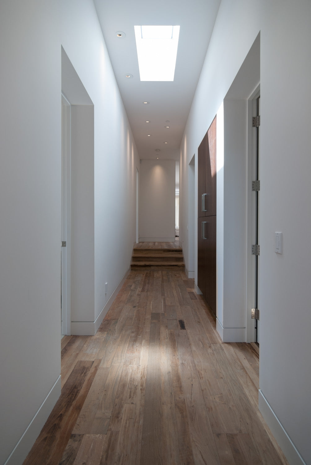 Long white hallway with skylights and continuous wood plank floor