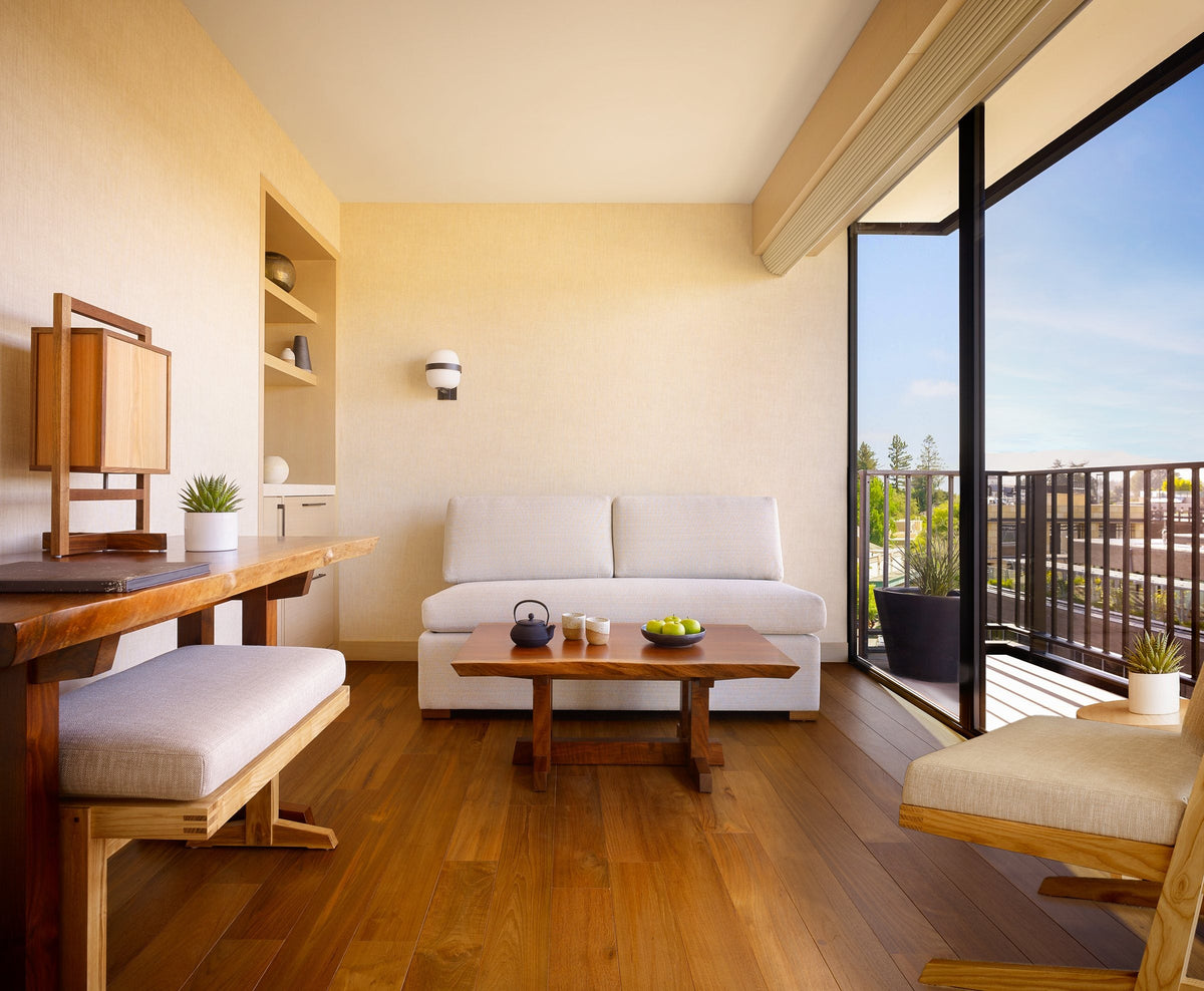 Warm wood floor in a suite with a sofa, desk and tall glazed doors to a balcony
