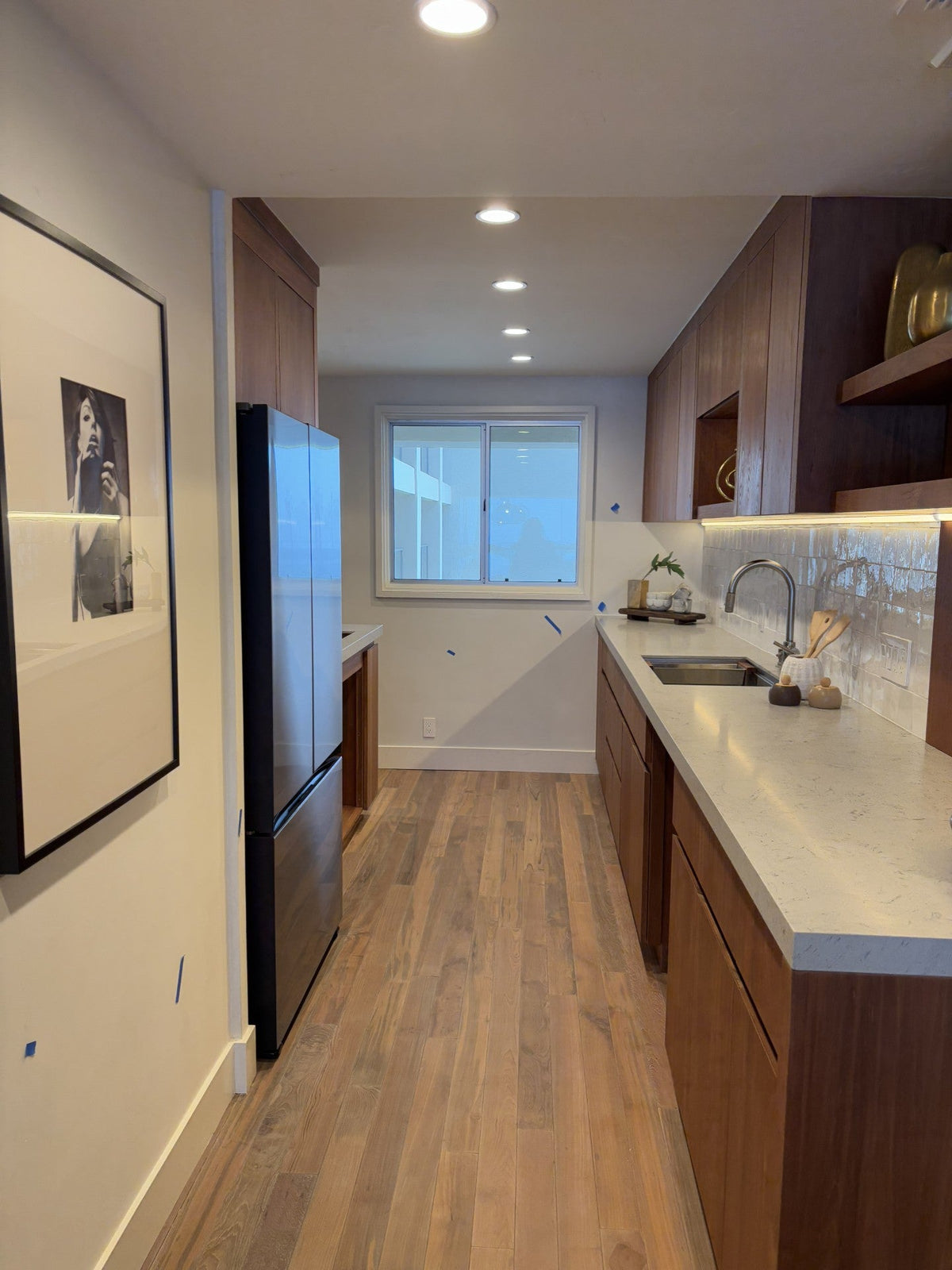 Narrow kitchen with wood flooring, white counters, and wood cabinets