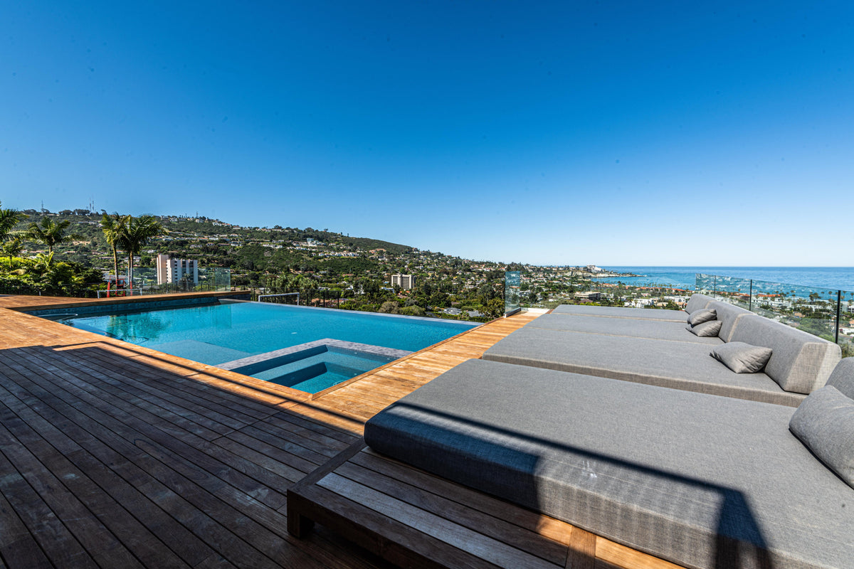 Poolside deck beside upholstered loungers and distant water