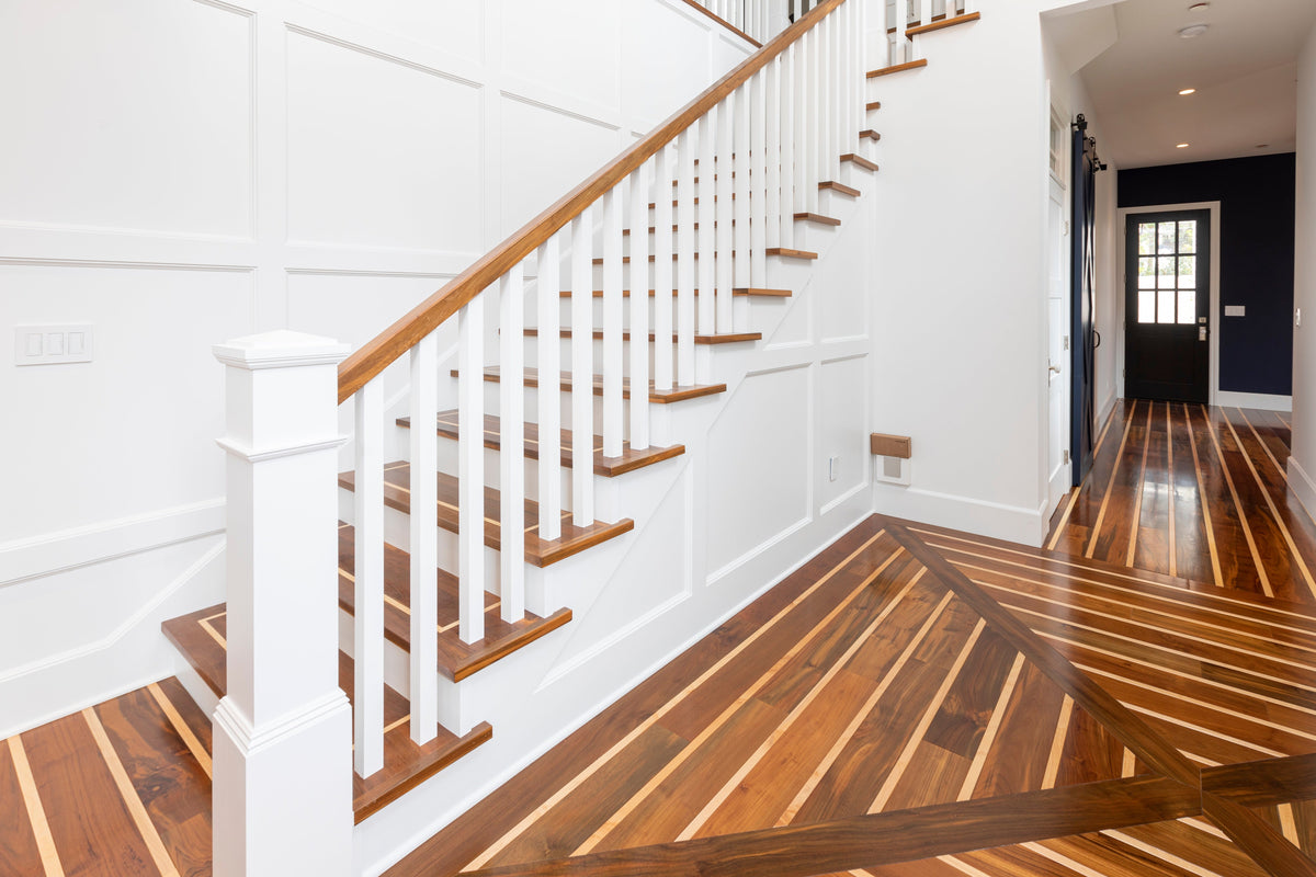 Striped wood floor with directional changes and borders at the foot of a white staircase