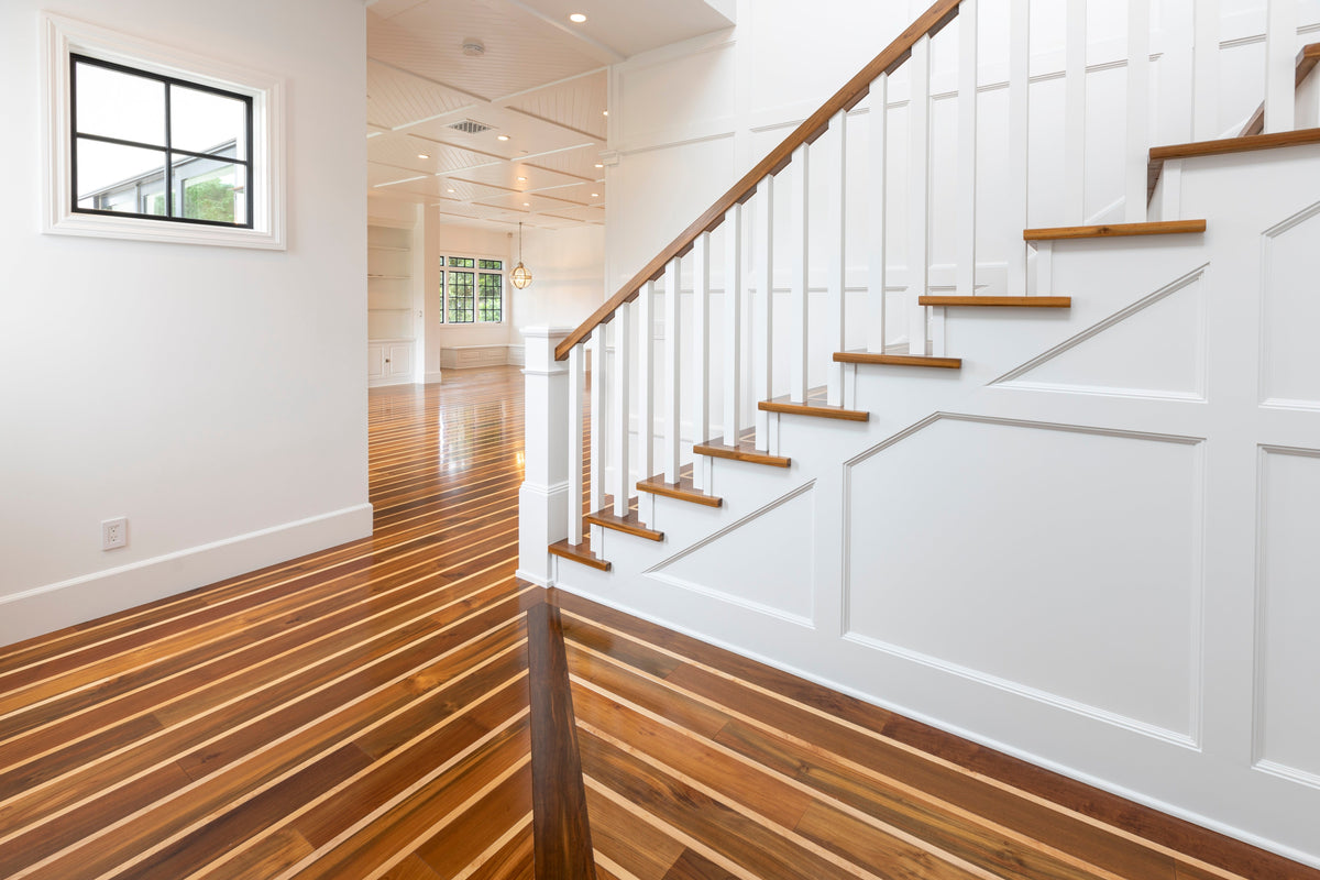 Glossy striped wood flooring beside white stairs and a hallway