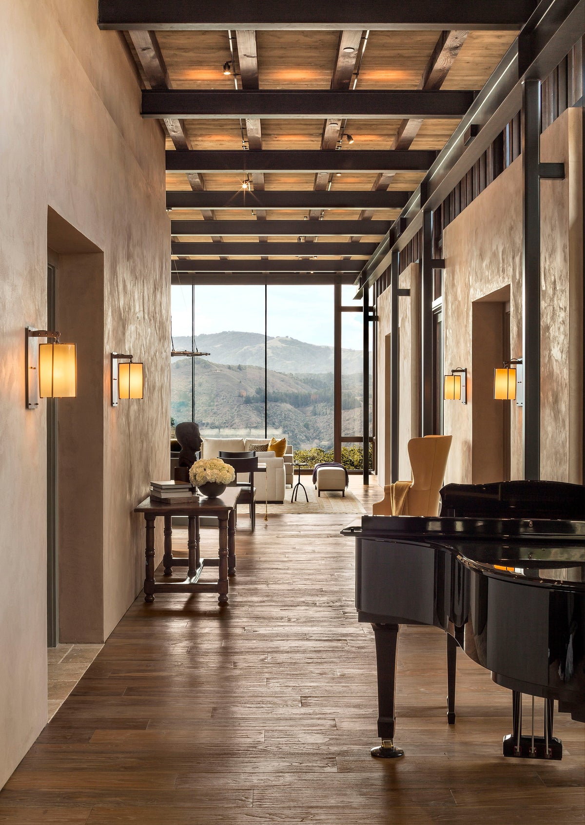 Long wood-floored room with a piano, exposed beams and tall windows