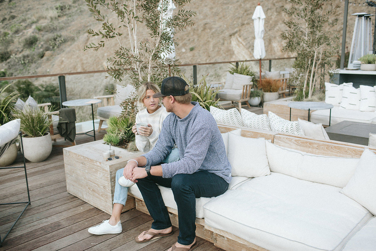 Pale outdoor seating and cushions sit on a weathered wood deck with potted plants