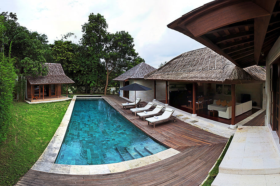 Timber decking surrounds a pool beside traditional thatched-roof buildings